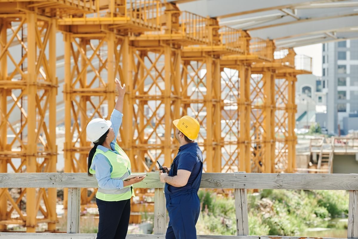 Project manager with tablet directing works alongside a tradesperson on a construction site